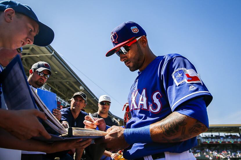 Texas Rangers outfielder Ian Desmond signs autographs for fans before a spring training game...