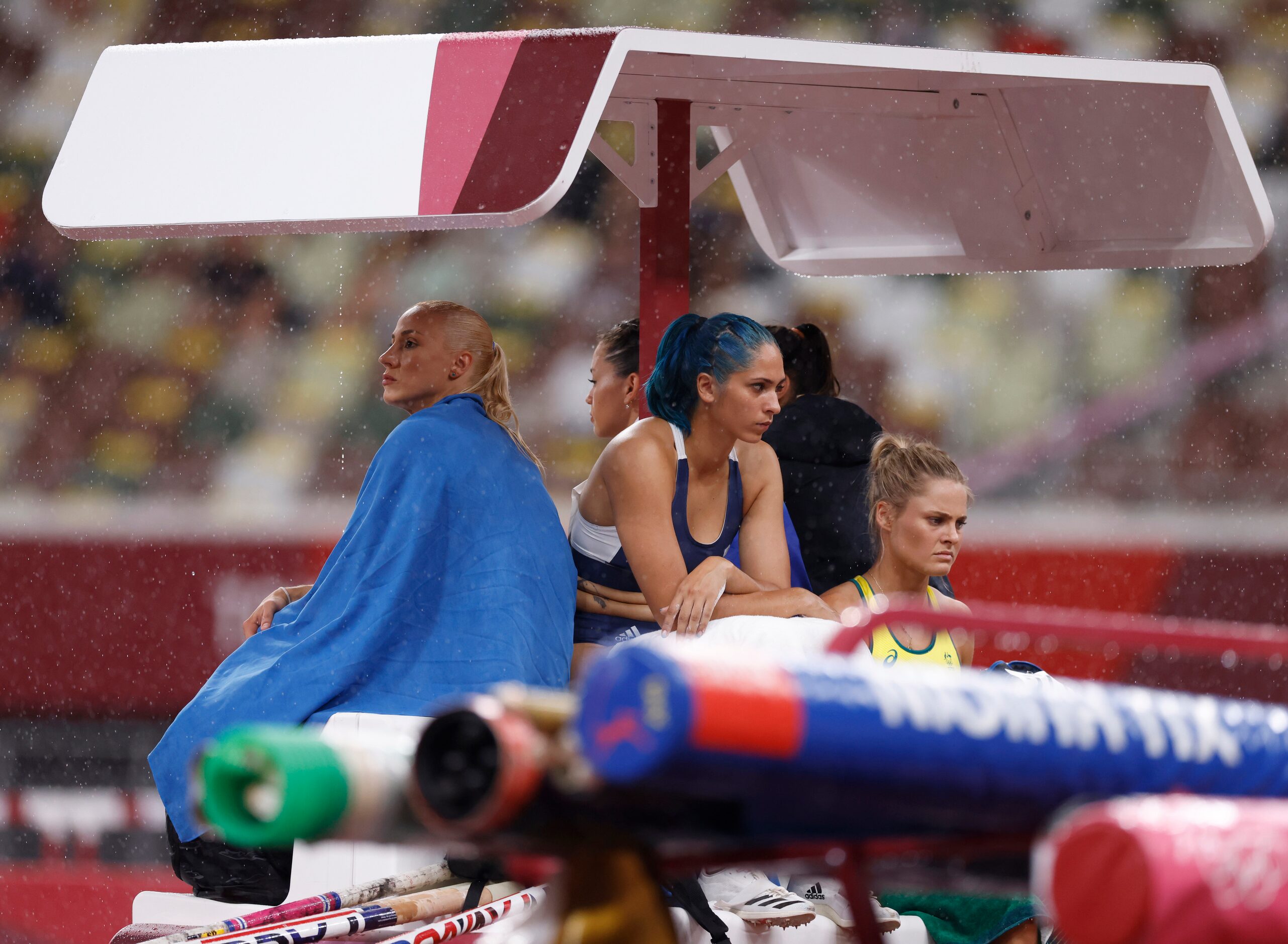 Pole vault athletes attempt to keep dry as it rains during a qualifying round during the...