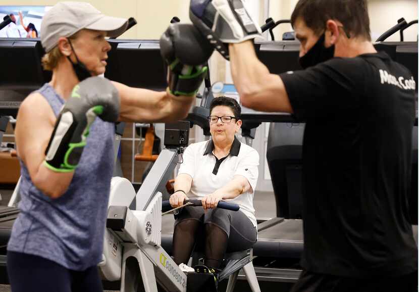 Gym member Melba Siebel of McKinney works out on a rowing machine while trainer Brent Wade...