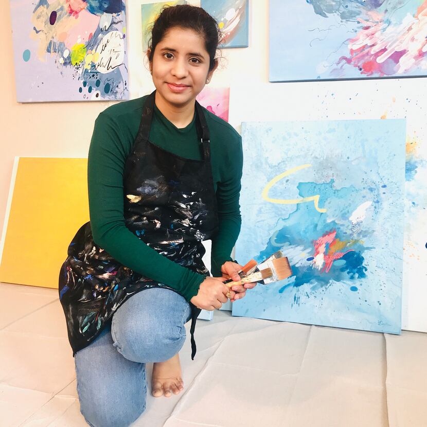 Artist Deepa Koshaley stands in front of a painting while holding a paintbrush