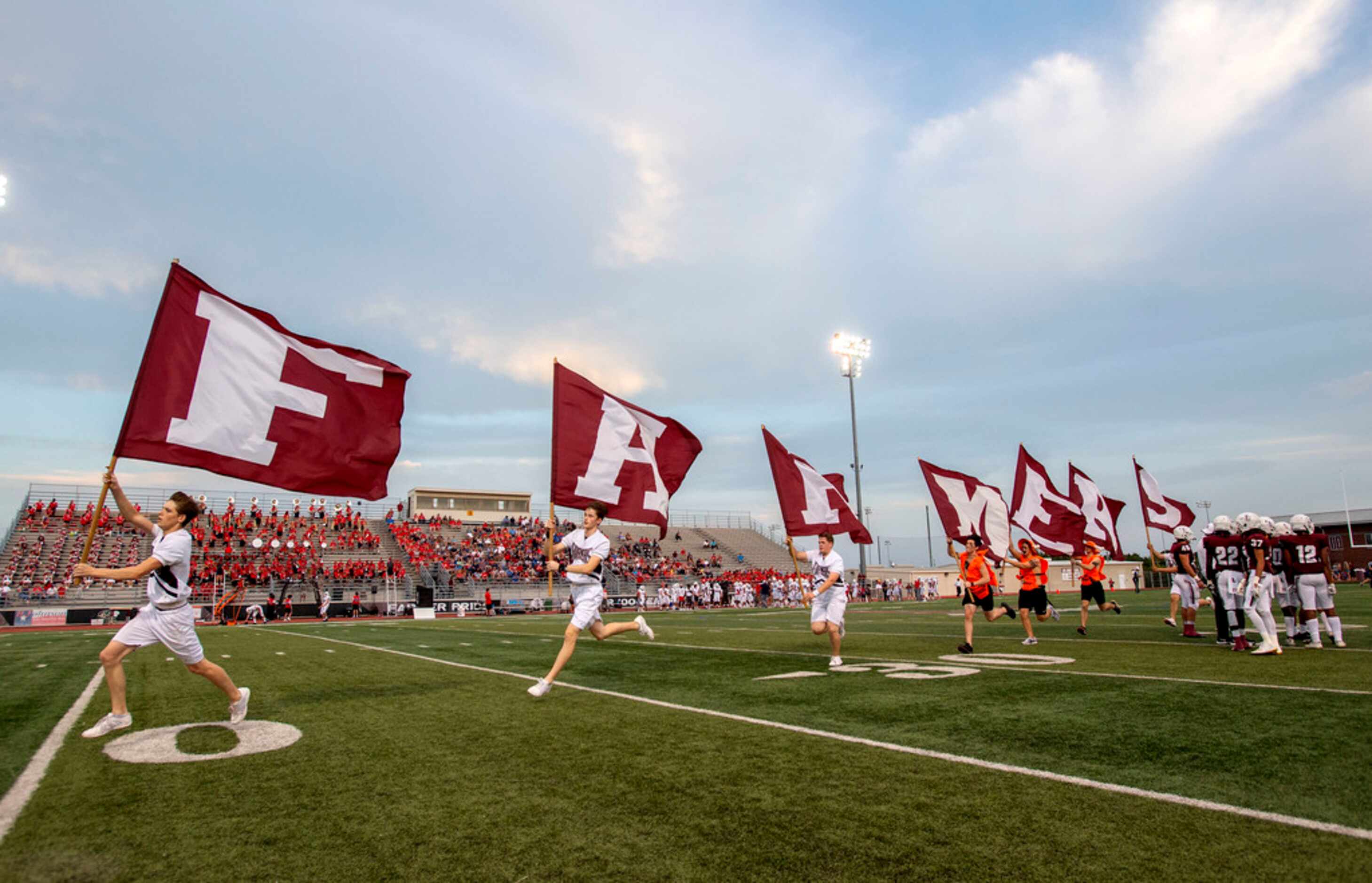 Lewisville cheerleaders run flags on the field after their team scored a touchdown against...