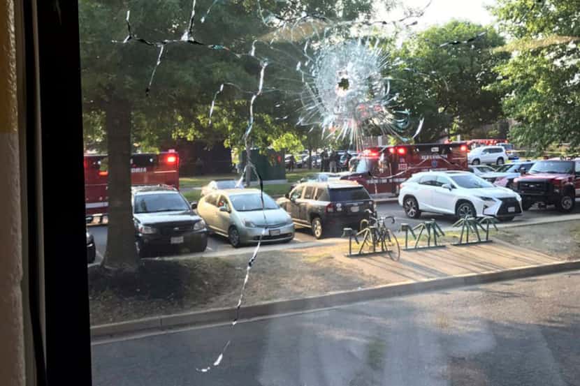 Emergency personnel are seen through a window with a bullet hole in Alexandria, Va.,...
