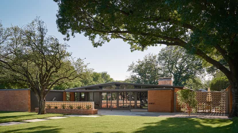 A renovated 1950s home with red brick sits on a tree-lined lot.
