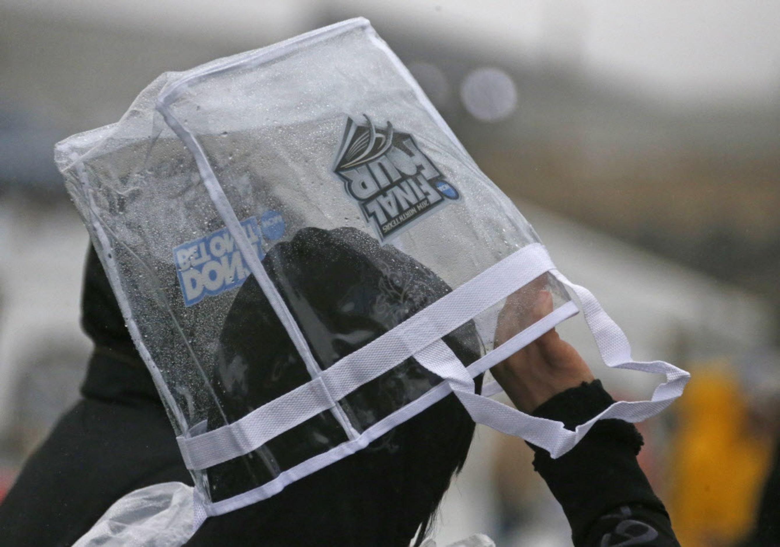 One music fan uses a give-away plastic bag to shield themselves from the rain during the...