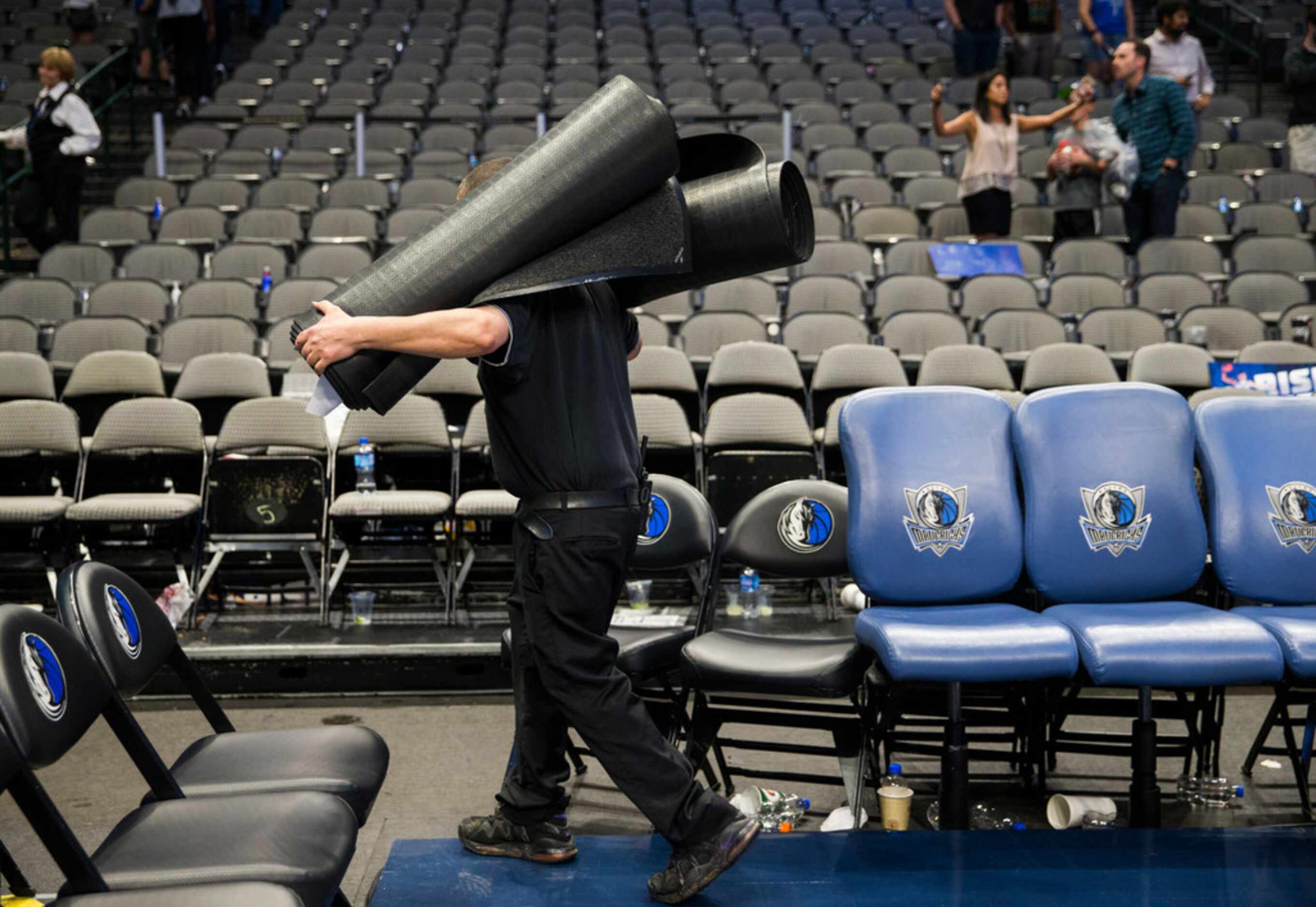 A worker removes rolled up carpets in front of the Mavs bench after the Dallas Mavericks...