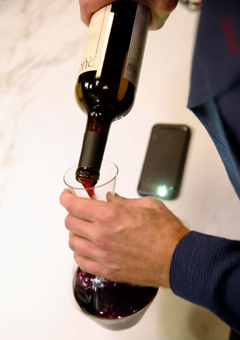 James Tidwell demonstrates how he uses the light on his smartphone while pouring wine into a...