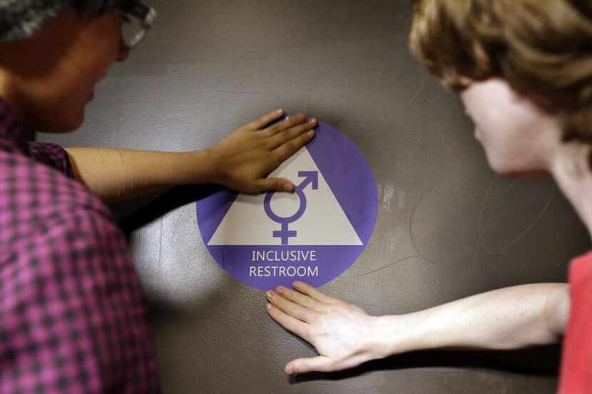 
Destin Cramer, left, and Noah Rice place a new sticker on the door at a gender neutral...