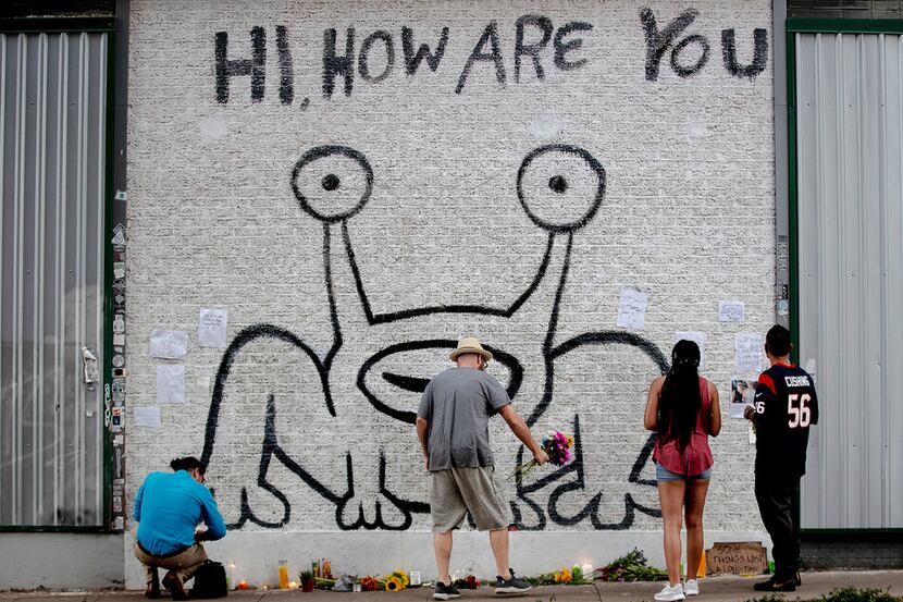 A man places flowers beneath the "Hi, How Are You" mural created by artist Daniel Johnston...