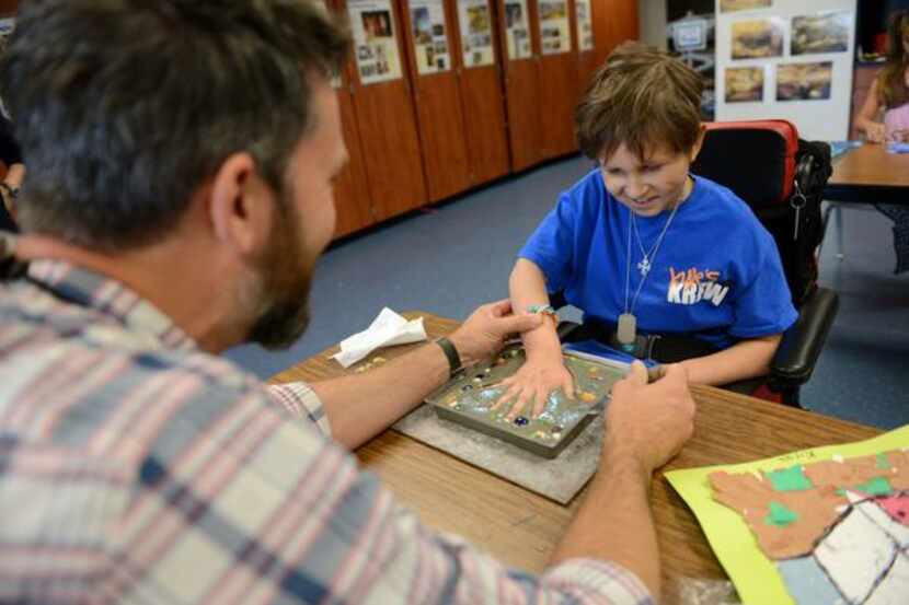 
Art teacher Justin Preston helps Kyle Murray, 10, imprint his hand into a concrete stepping...