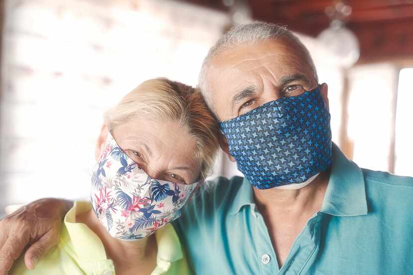 Una pareja mayor en máscaras de la cara juntos y sonriendo a la cámara.