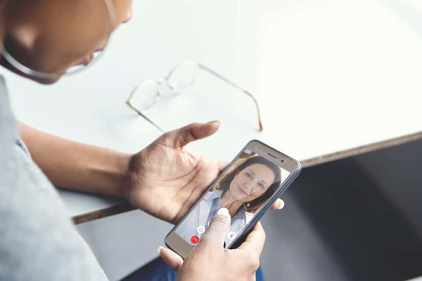 A woman holds a phone for a video call with a Teladoc specialist displayed on the screen.