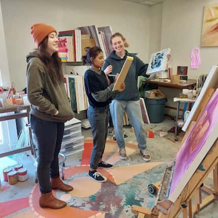 Inside an artist's studio three artists observe works propped on easels.