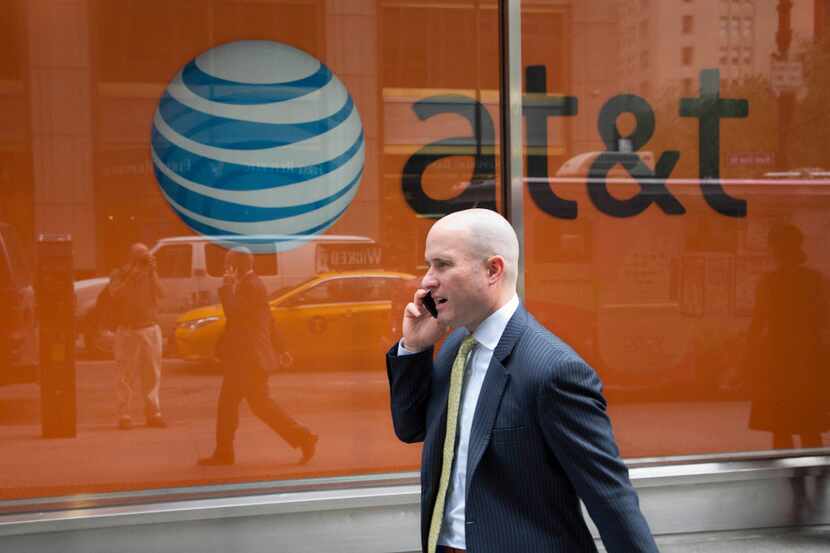 In this Tuesday, June 23, 2015, photo, a man using a mobile phone walks past an AT&T store,...