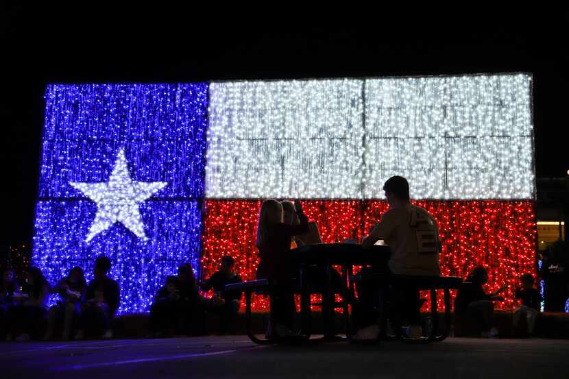 Guests enjoy food and drink in front of a Texas flag lighted sculpture at Luminova Holidays...