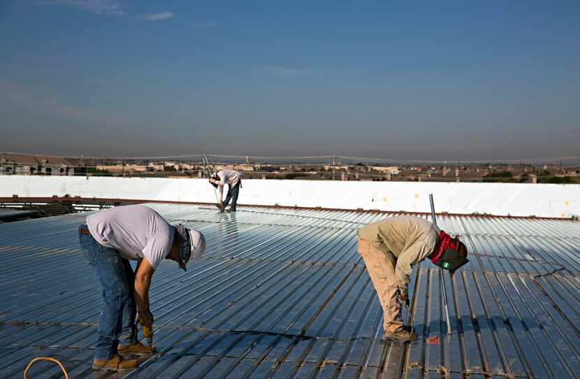 Workers attach metal panels to the roof at the new Memorial High School on Frisco Street...