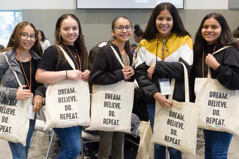 A group of young students poses together at Innovate(her), holding tote bags that read...