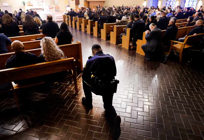 A Dallas Police officer takes a knee behind the last pew during the funeral mass for fellow...