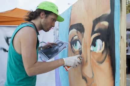 Daniel Black spray paints a portrait near the Audacity Brew House main stage on the final...