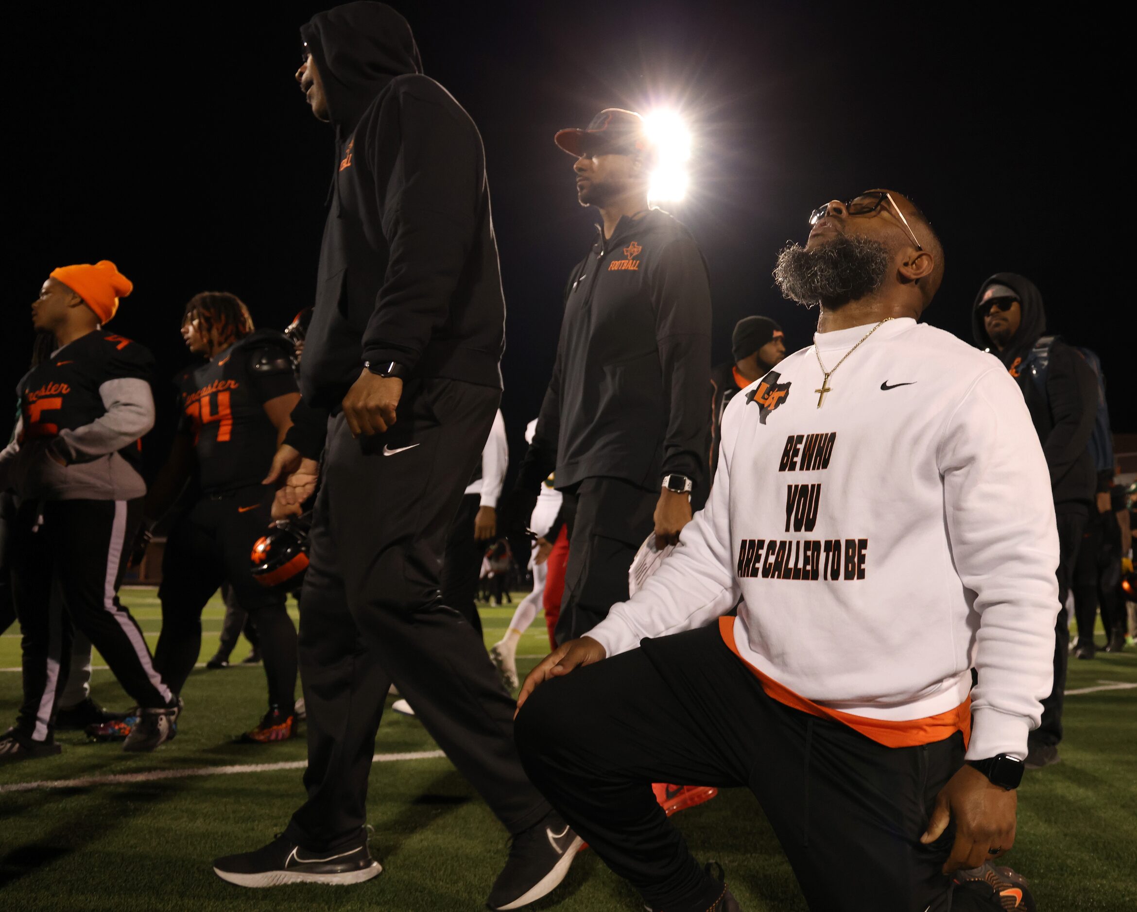 Lancaster head coach Leon Paul takes a knee to pray at midfield as his assistant coaches and...