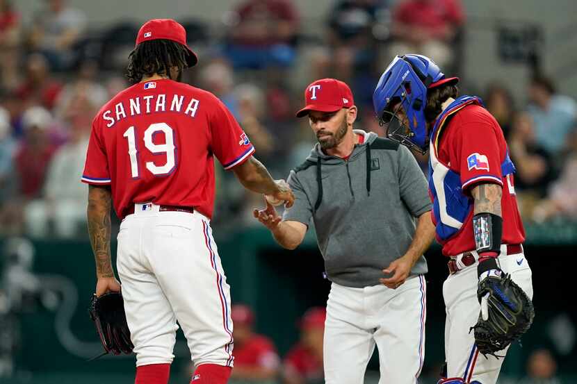 Texas Rangers' Dennis Santana (19) turns the ball over to manager Chris Woodward, center, as...