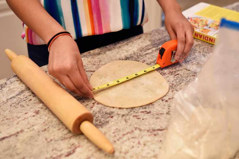 Meha Elhence, 21, uses a measuring tape to measure the appropriate size for dough while...