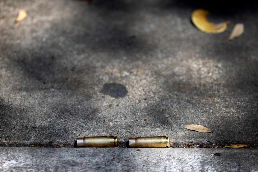 Shell casings settled in a sidewalk crease near a memorial for two shooting victims Friday...
