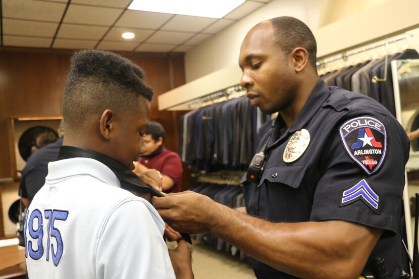 Arlington police Cpl. Damien Gary teaches Isiah Austin how to tie a necktie at a formalwear...