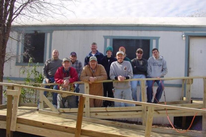 A group of volunteers with GLC’s Project Wheelchair Ramp help a wheelchair-bound teen whose...