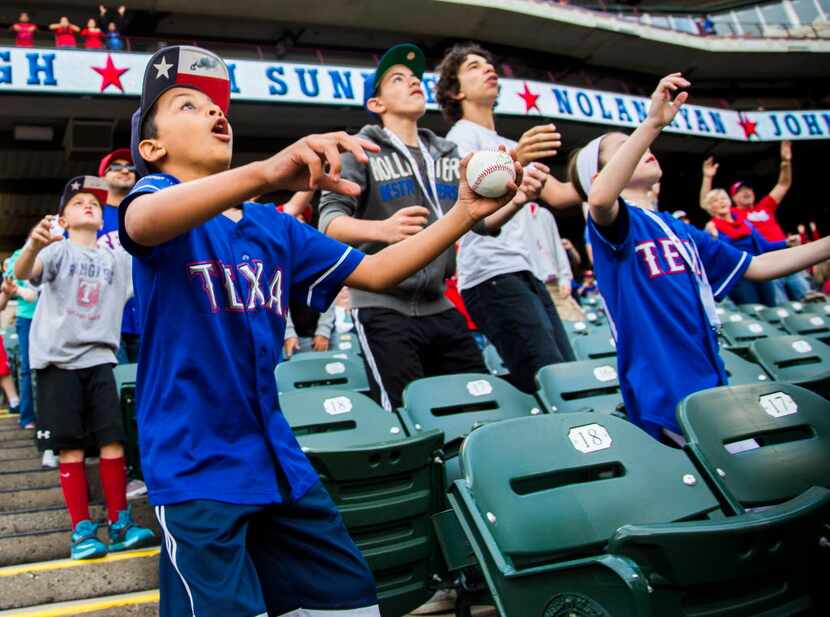 Young Texas Rangers fans reach to catch a t-shirt tossed from the field before of their game...