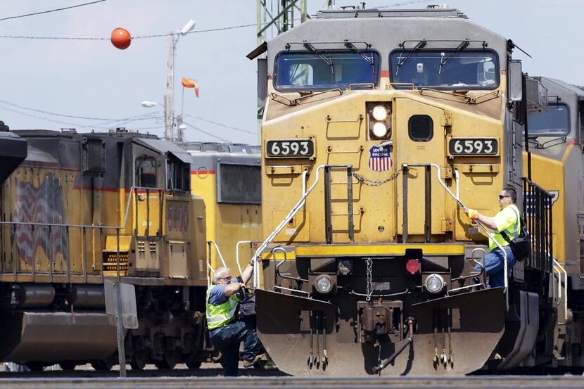 A train operator (left) dismounts a Union Pacific locomotive while another operator climbs...