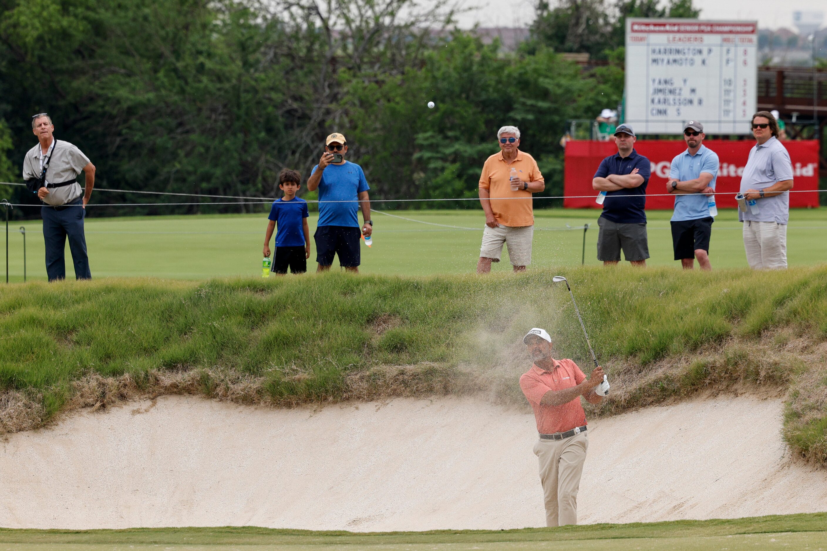 Fans watch as Arjun Atwal of India hits out of a bunker on the 18th hole during the first...