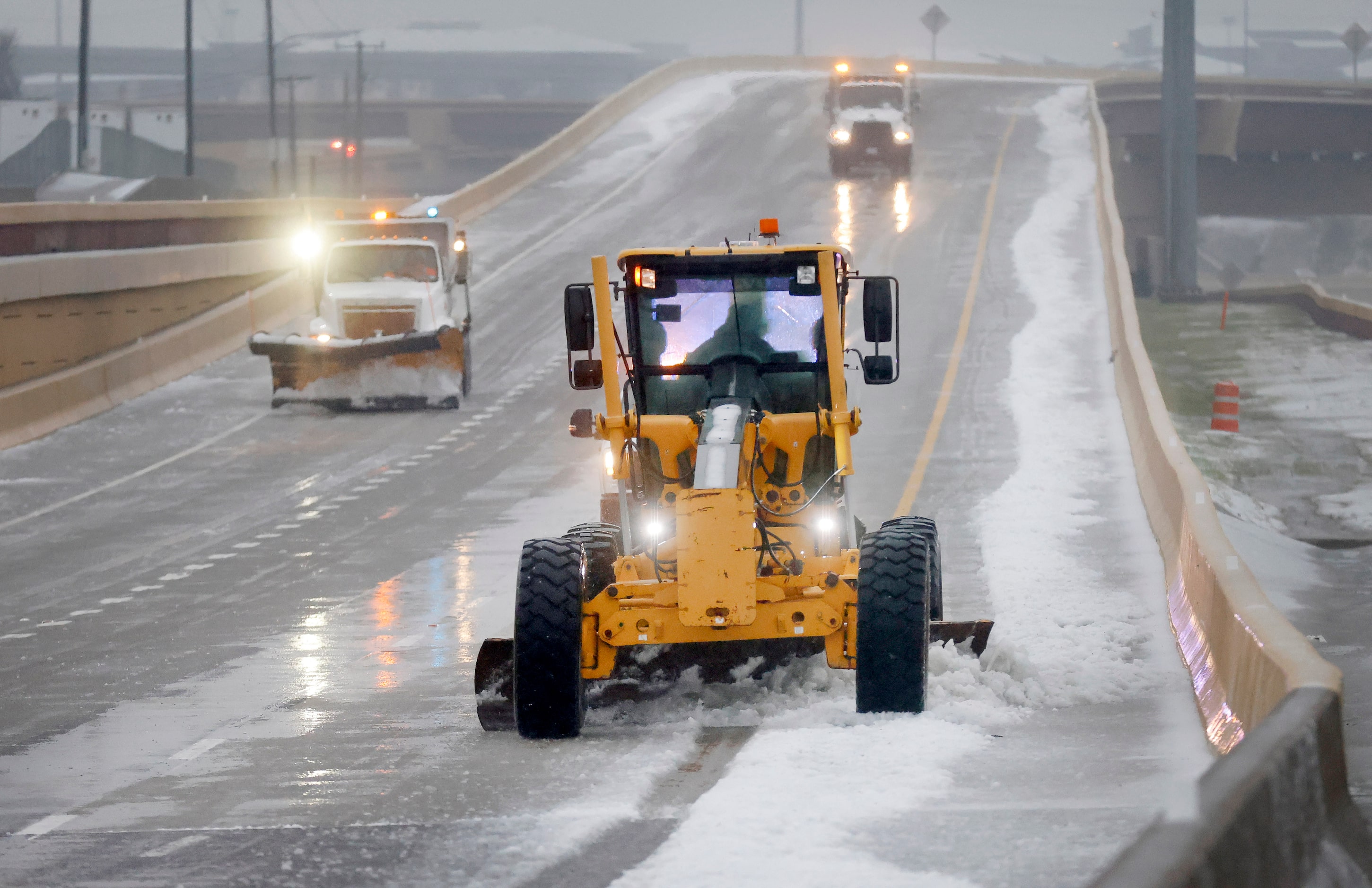 A grader plows sleet off of a bridge and entrance ramp from eastbound SH 114 to John...