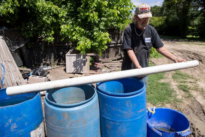 Richard Shivers shows the tube he uses to fill barrels with water from a water container...