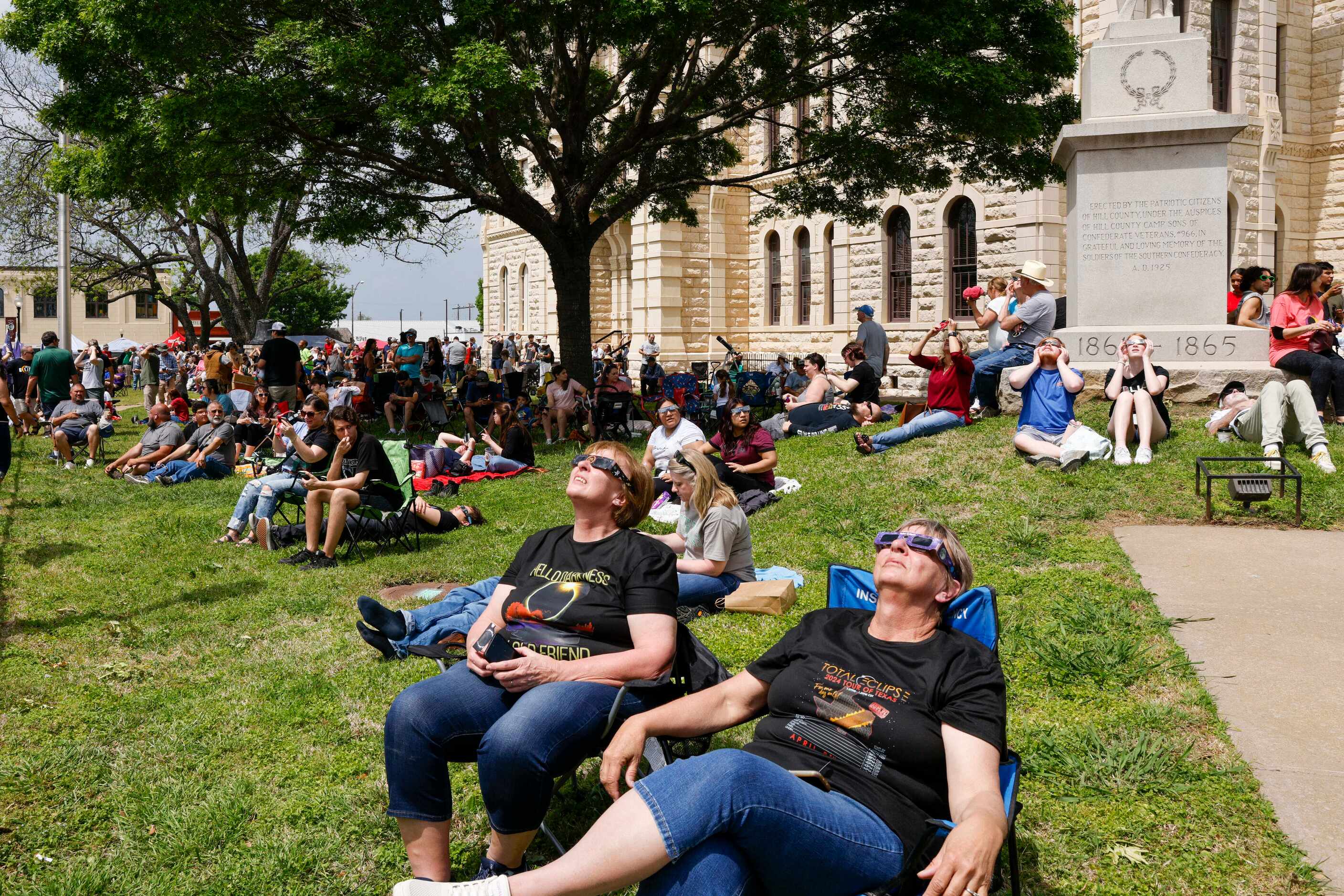 People sit outside the Hill County Courthouse to watch a partial solar eclipse, Monday,...