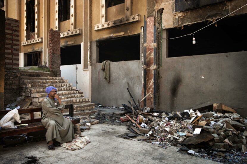 An Egyptian Coptic Christian sits on a bench near debris that remains in the courtyard of...