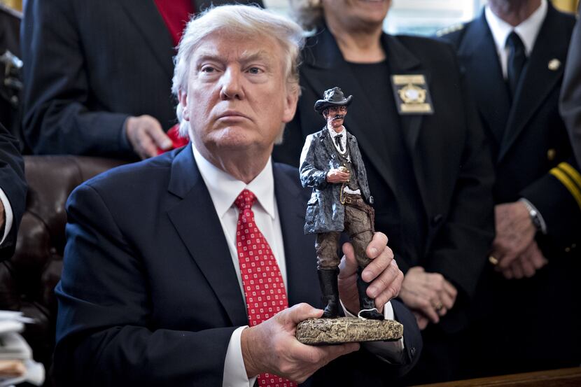 Trump holds up a statue he received as a gift while meeting with sheriffs in the Oval...