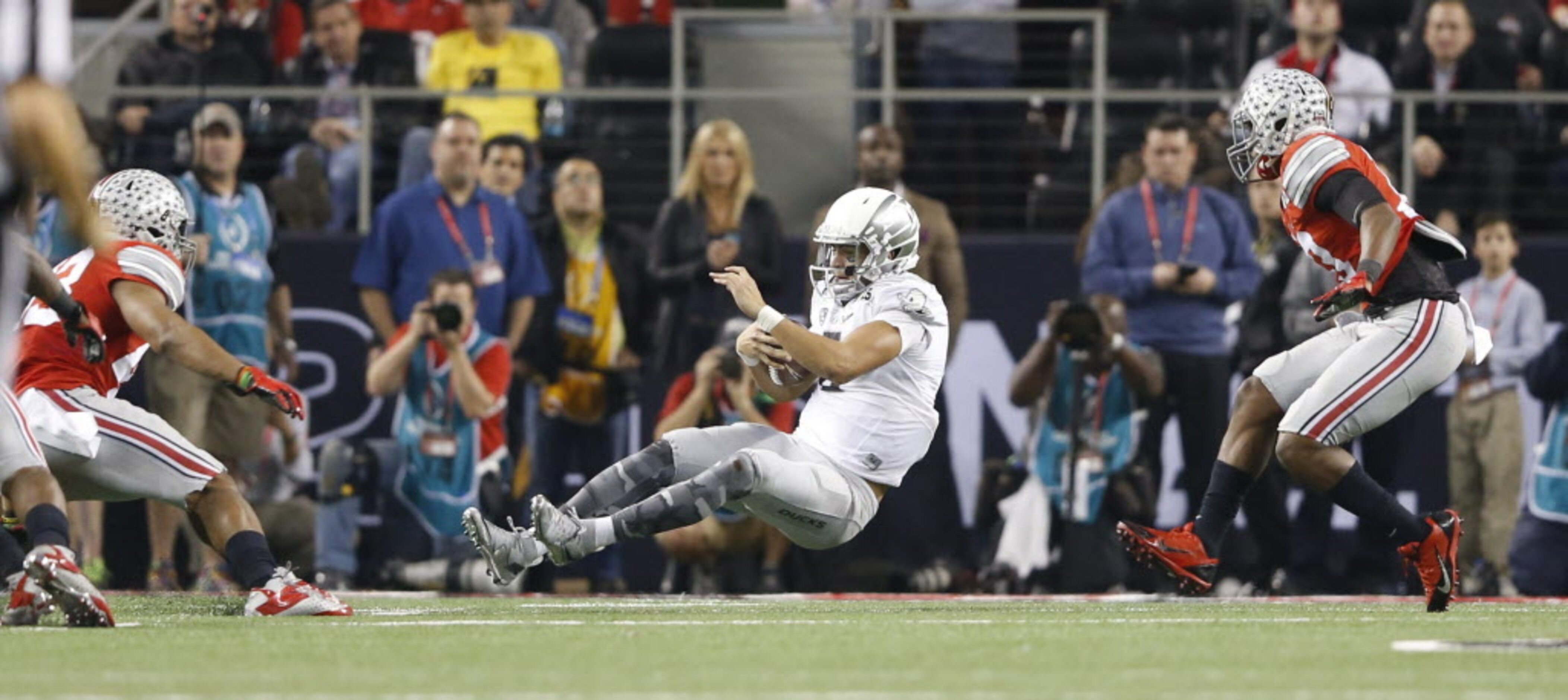 Oregon Ducks quarterback Marcus Mariota (8) slides to a stop in front of two Ohio State...