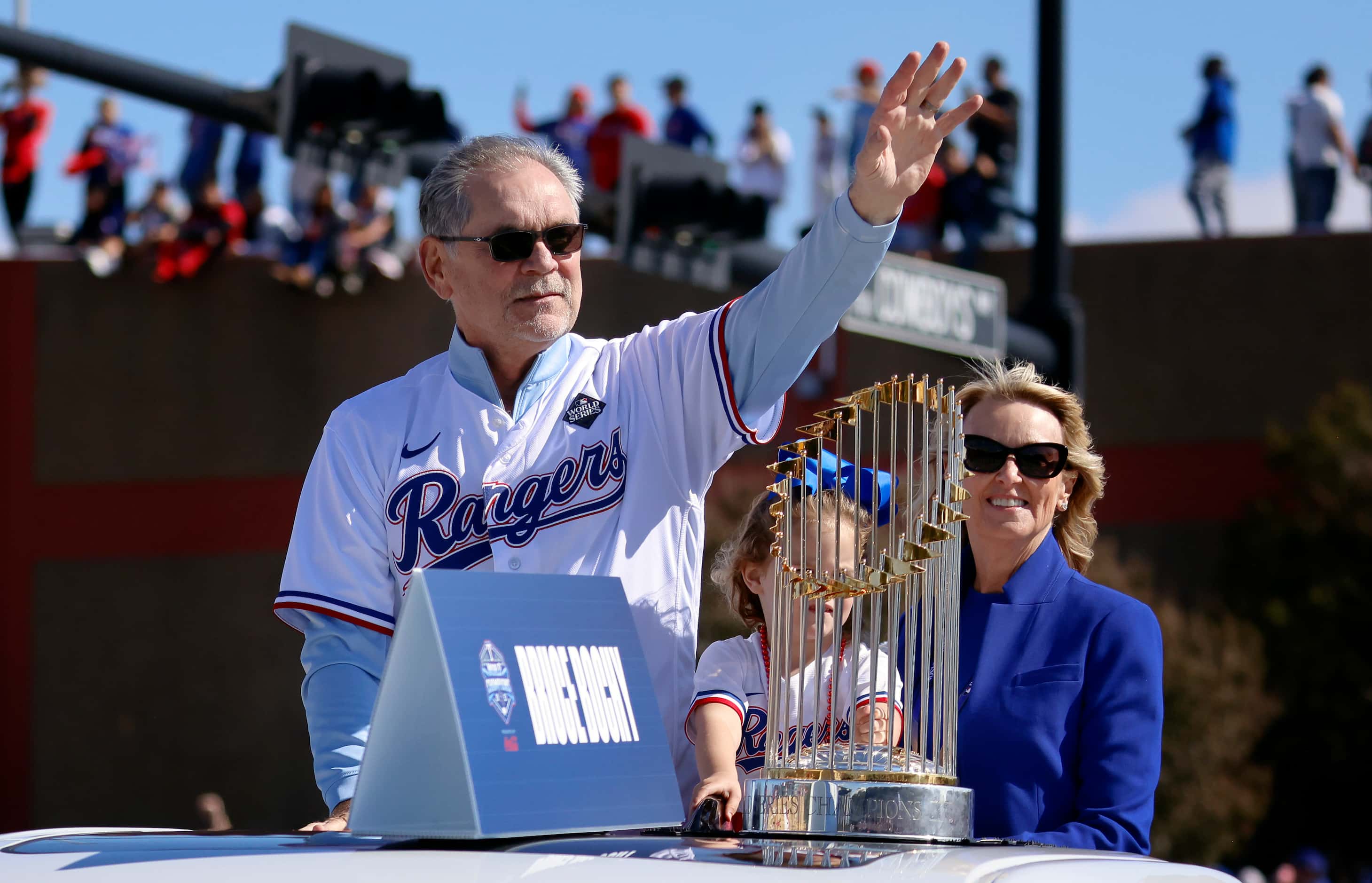 Riding with the Commissioner's Trophy, Texas Rangers manager Bruce Bochy, left, waves to...