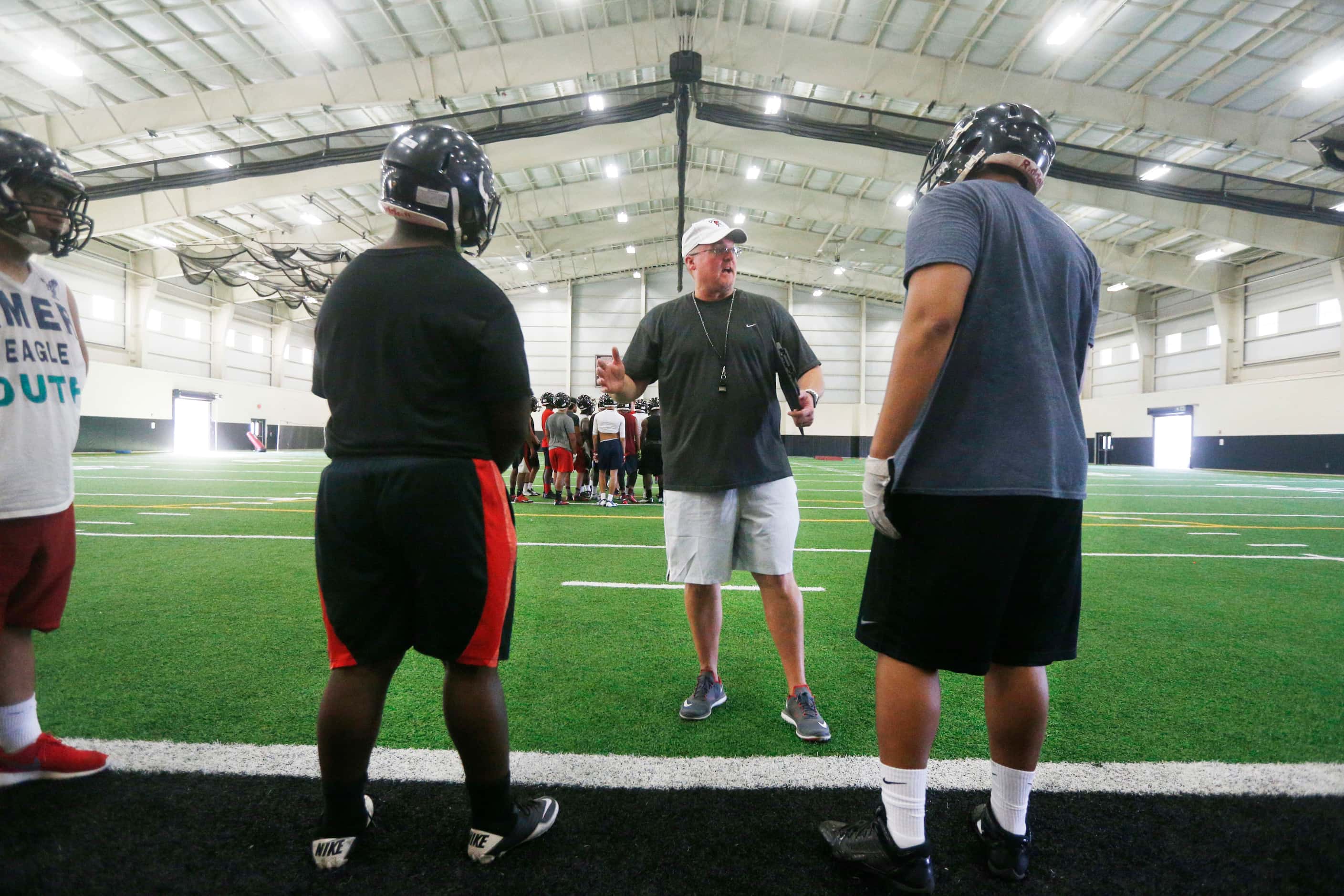 Coach Chris Jensen talks to offensive linemen during Euless Trinity's first day of football...