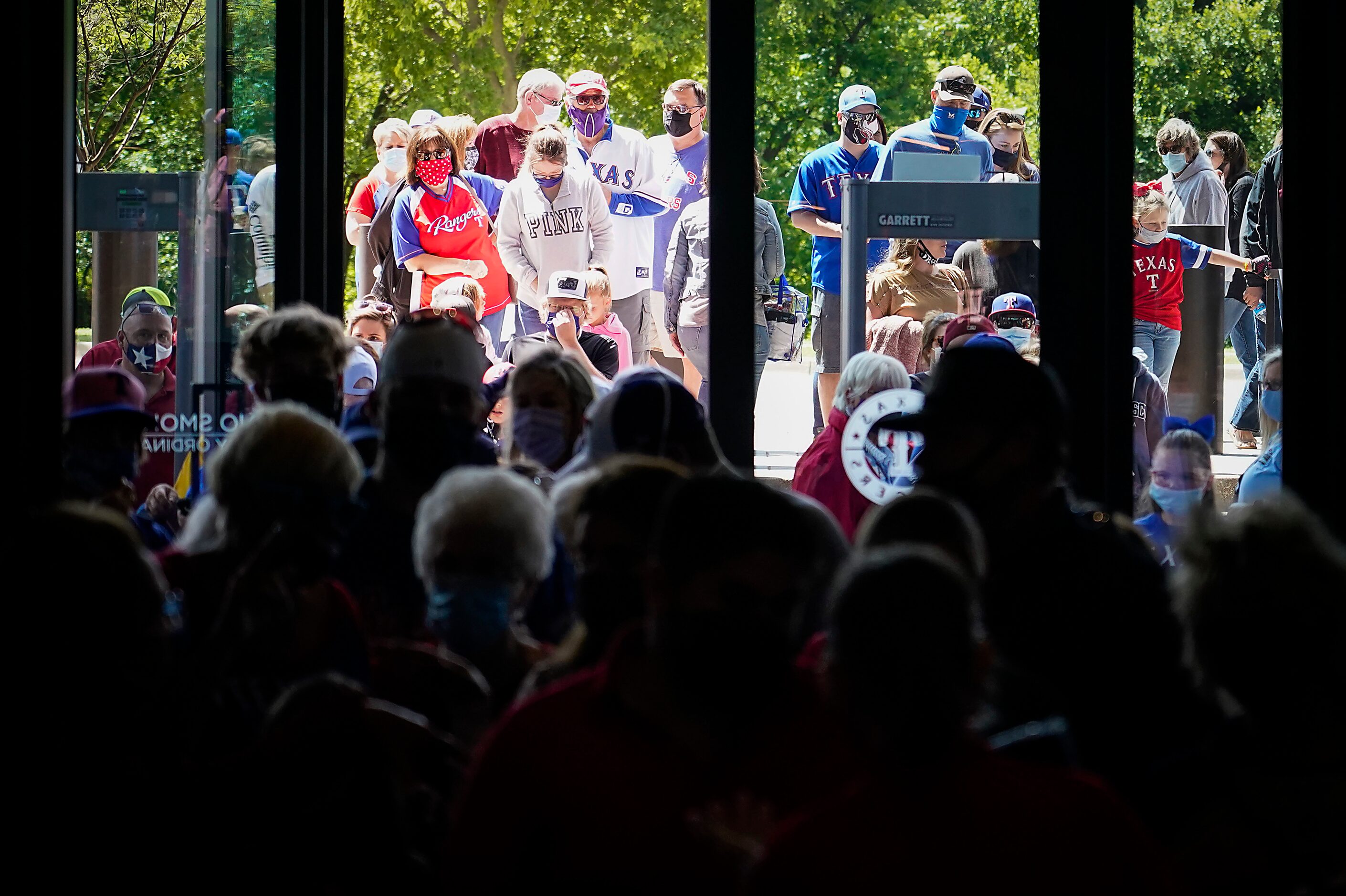 Fans wait in line to go enter the stadium before a game between the Texas Rangers and the...