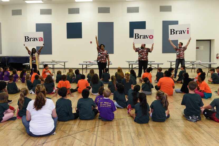 Elementary aged children sit on the floor while instructors hold up signs saying "Brava,...