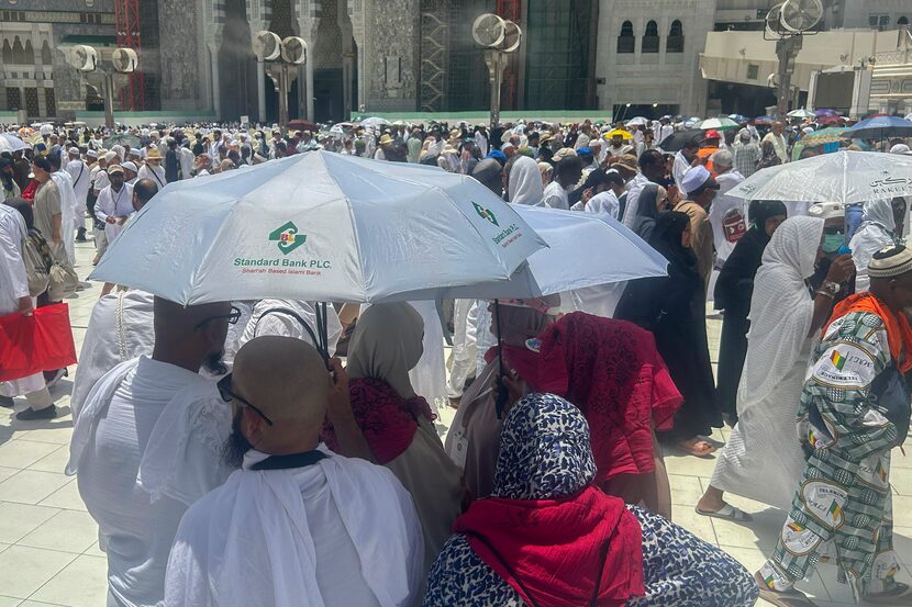 A group of pilgrims share umbrellas to protect themselves from the heat as they leave after...