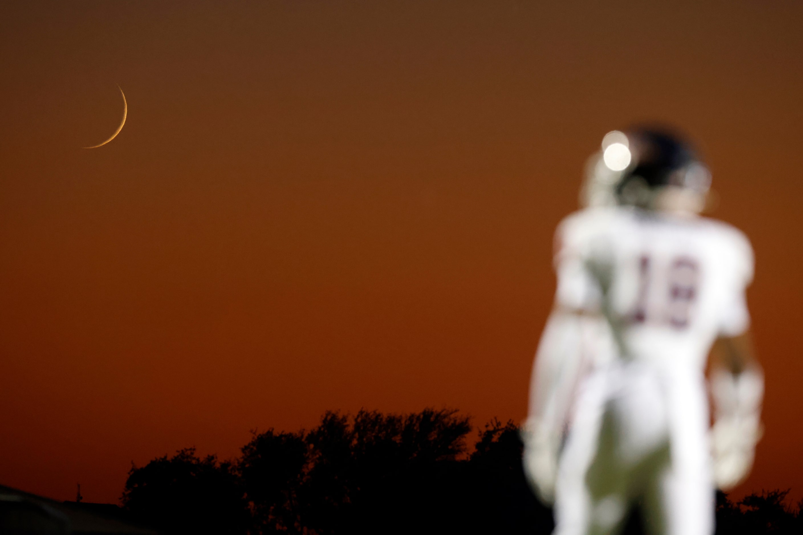 A Denton Ryan player stands on the field as the moon sets during the first half of a...