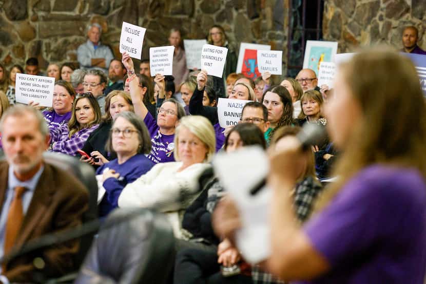 People raise signs opposing banning books about gender fluidity during a Keller school board...