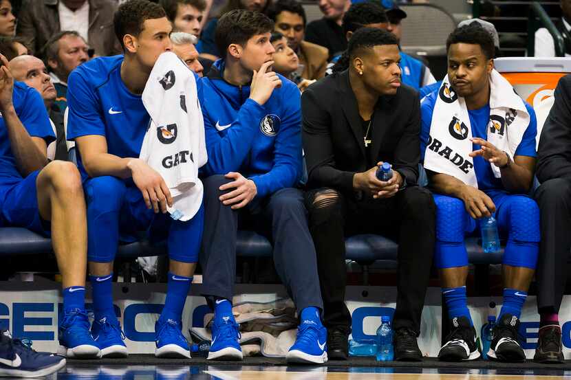 Dallas Mavericks guard Dennis Smith Jr. watches from the bench in street clothes as he talks...