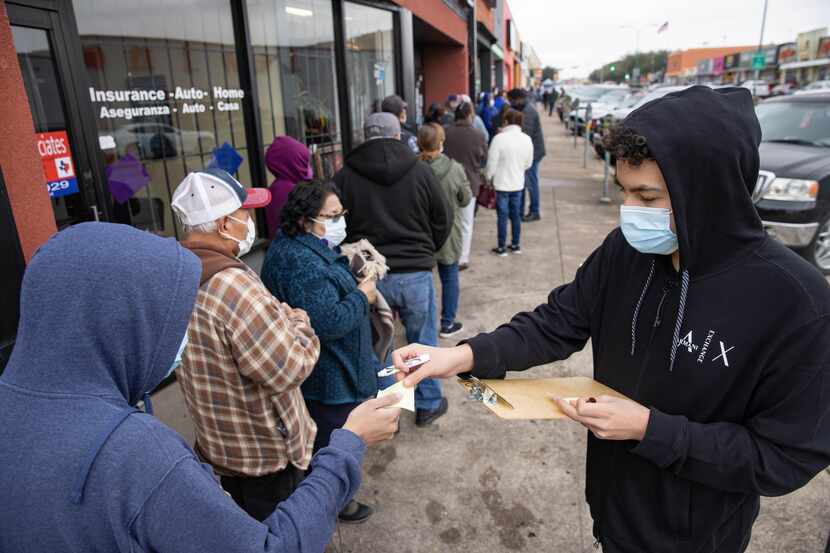 Volunteer Favian Hernandez (right) hands out numbers to the 187 person waiting in line for a...