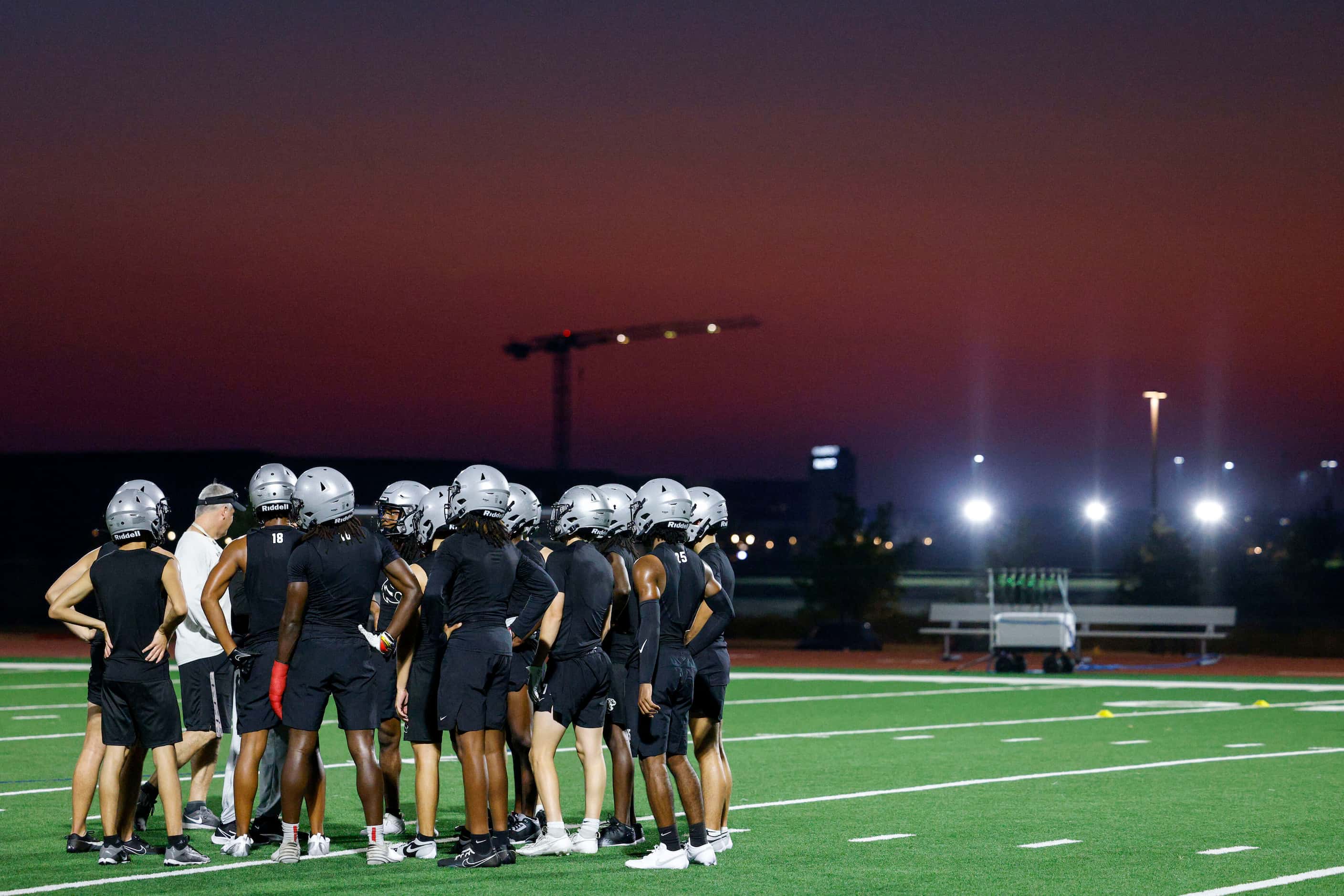 Players huddle on the field during a football practice before sunrise at Panther Creek High...