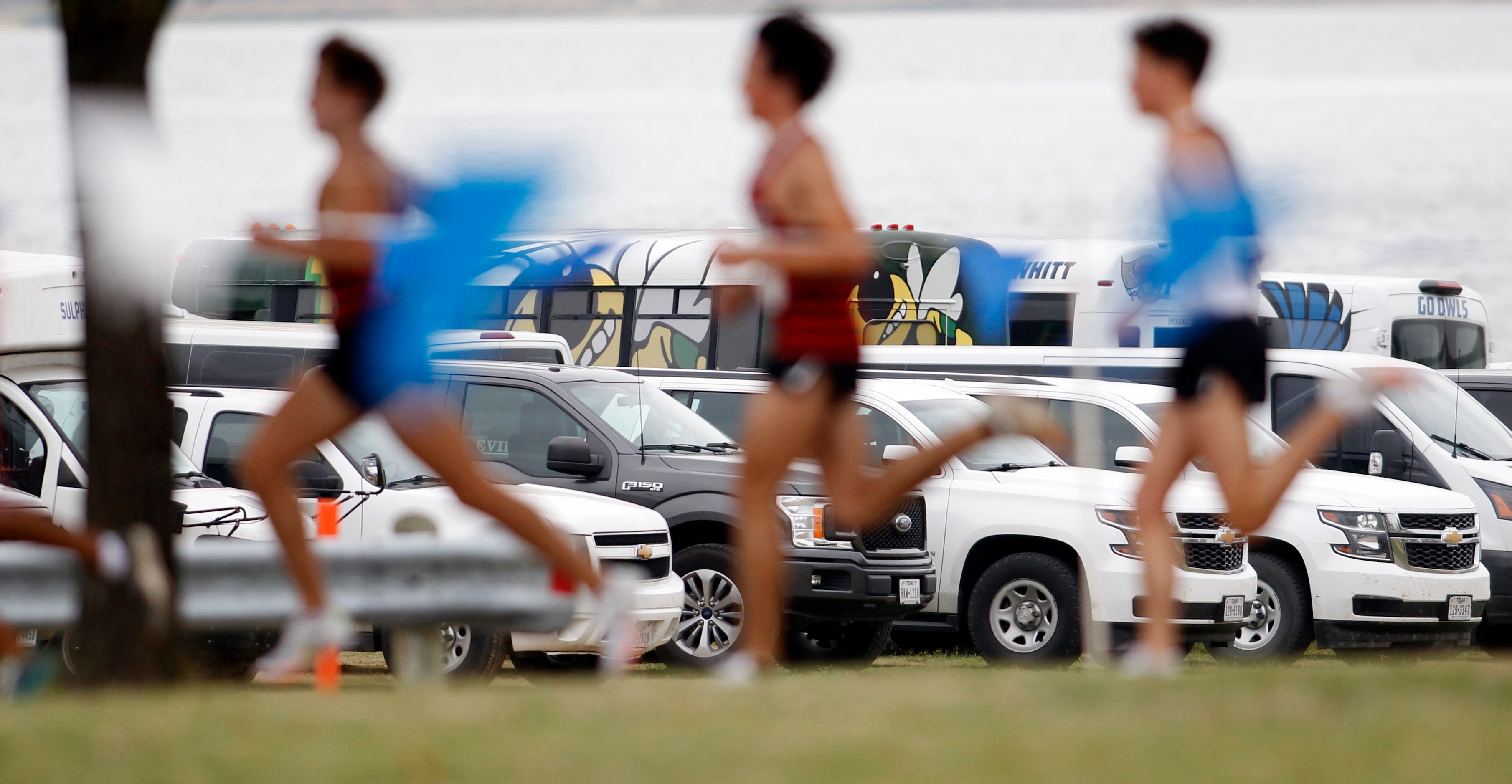 A group of runners in the Class 5A Region 2 boys race pass by a large parking lot full of...