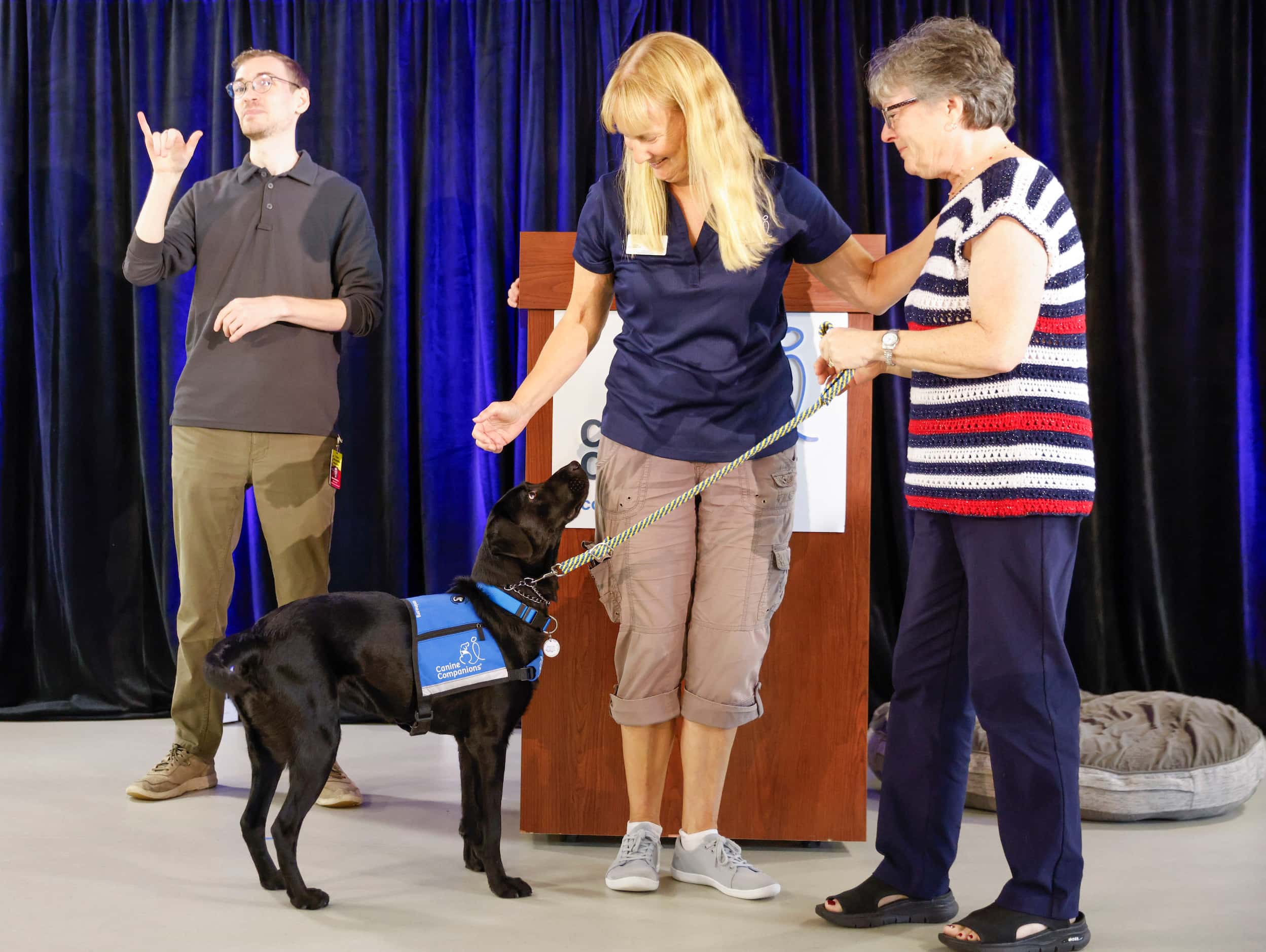 Trainer Aimee Schildt (center) reaches to pet Dakota, dog of veteran Kathy Schneider (right)...