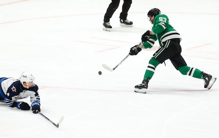 Winnipeg Jets defenseman Neal Pionk (left) reaches to block a shot of Dallas Stars center...